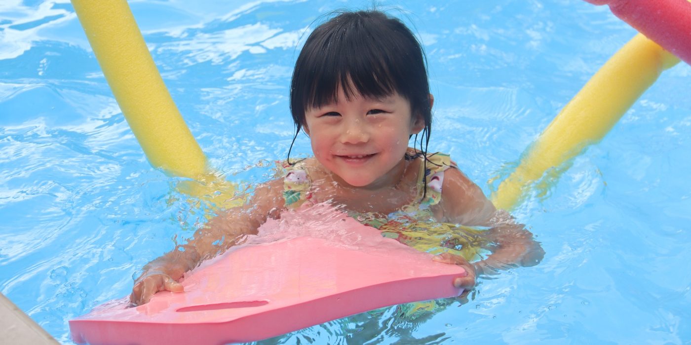 A child swimming with a kickboard during a uKids session