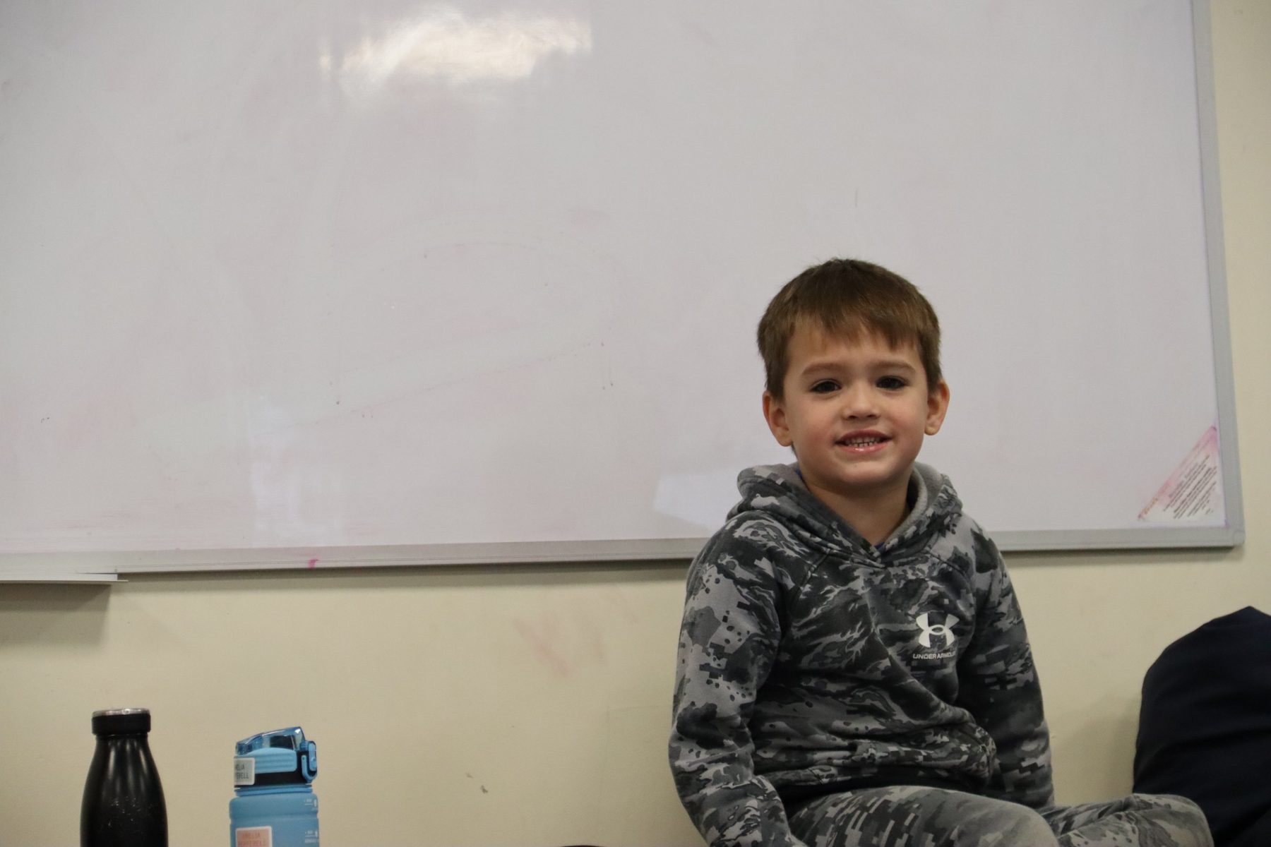 A smiling child sitting in front of a whiteboard at uKids club