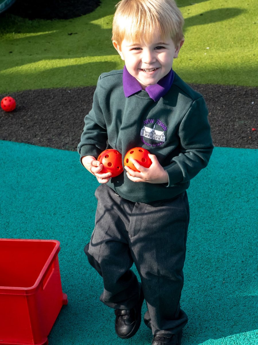 Smiling boy carrying two balls in the New Town Primary School playground