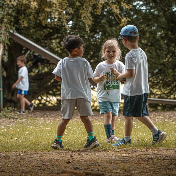 Children playing together outdoors under the trees at uKids camp
